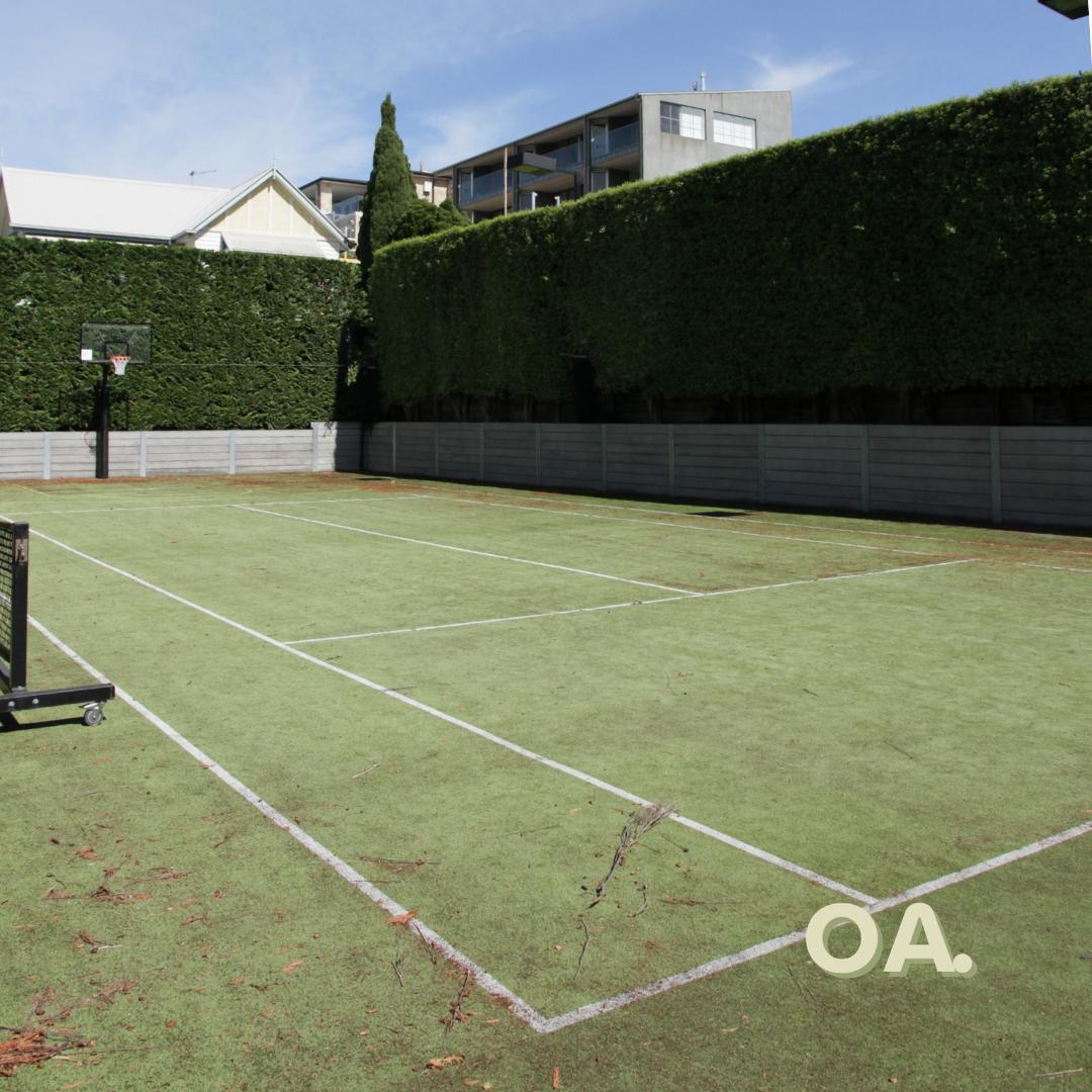 The same walled grass court before, worn and dirty with faded lines